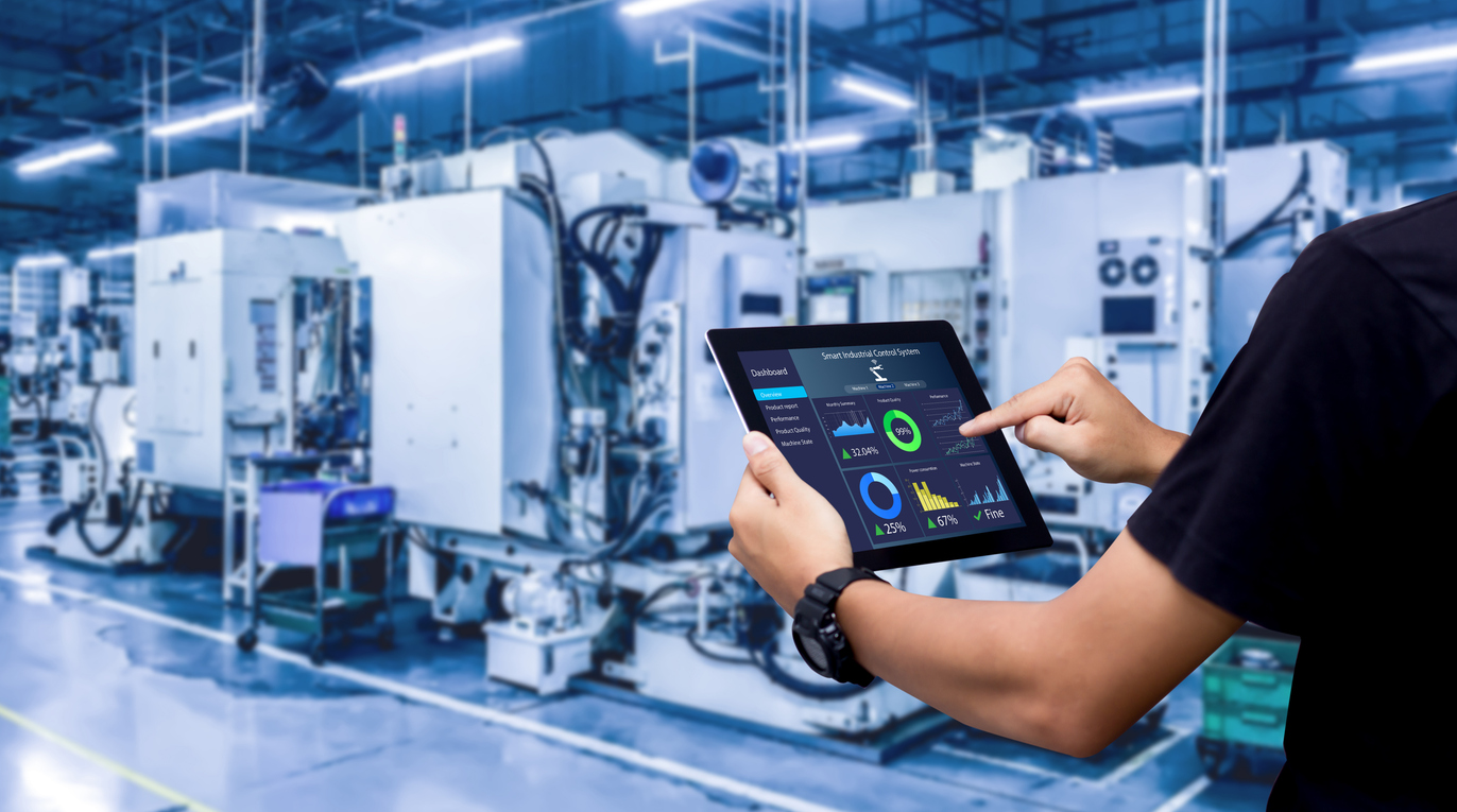 Image of a technician holding a tablet with various metrics and measurements, with large machines filling the background.