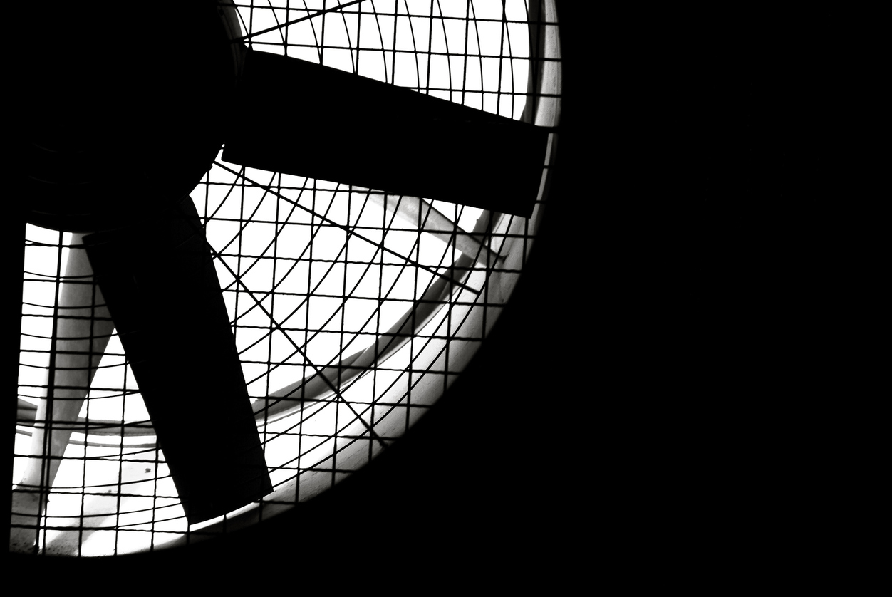 Black and white shot of an industrial fan turbine behind a metal grate